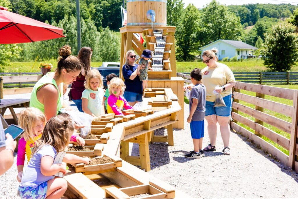 A group of kids and adults sifting mining rough at the gem mining sluice below the water tower at Fox's High Rock Farm in Logan, Ohio